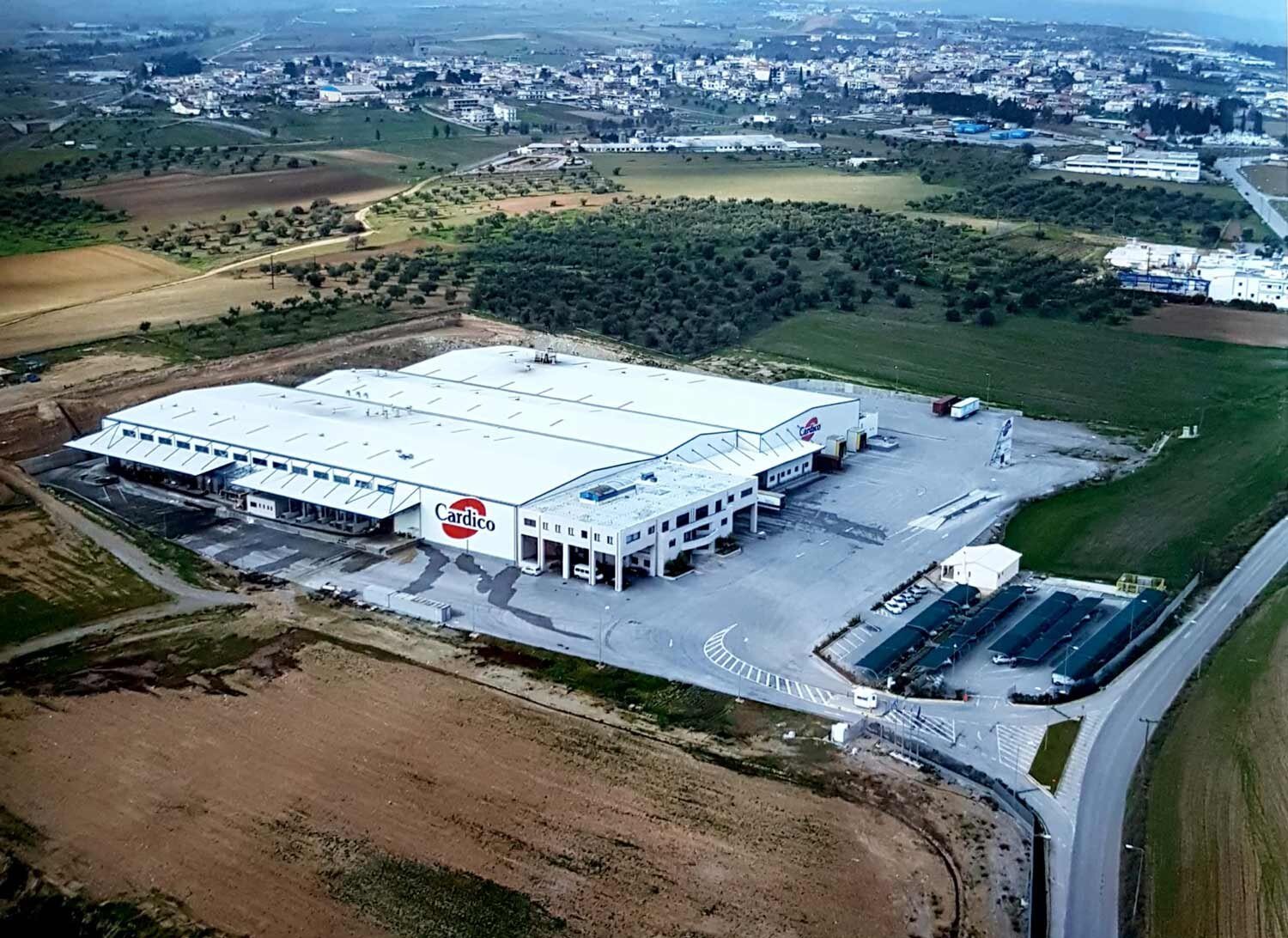 Αεροφωτογραφία του εργοστασίου της Cardico στο Σχηματάρι, με την επιγραφή Cardico στην πρόσοψη, ανάμεσα σε χωράφια και ελαιώνες.